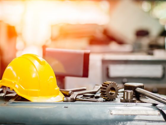 yellow hardhat with tools on a table with a machinery factory in the background